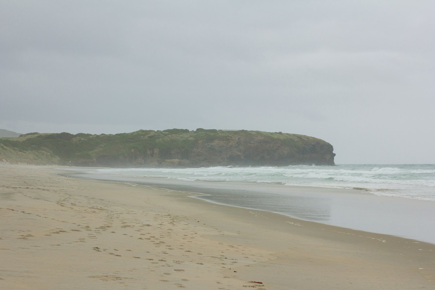 Sandy beach with gentle ocean waves meeting a vegetated headland.