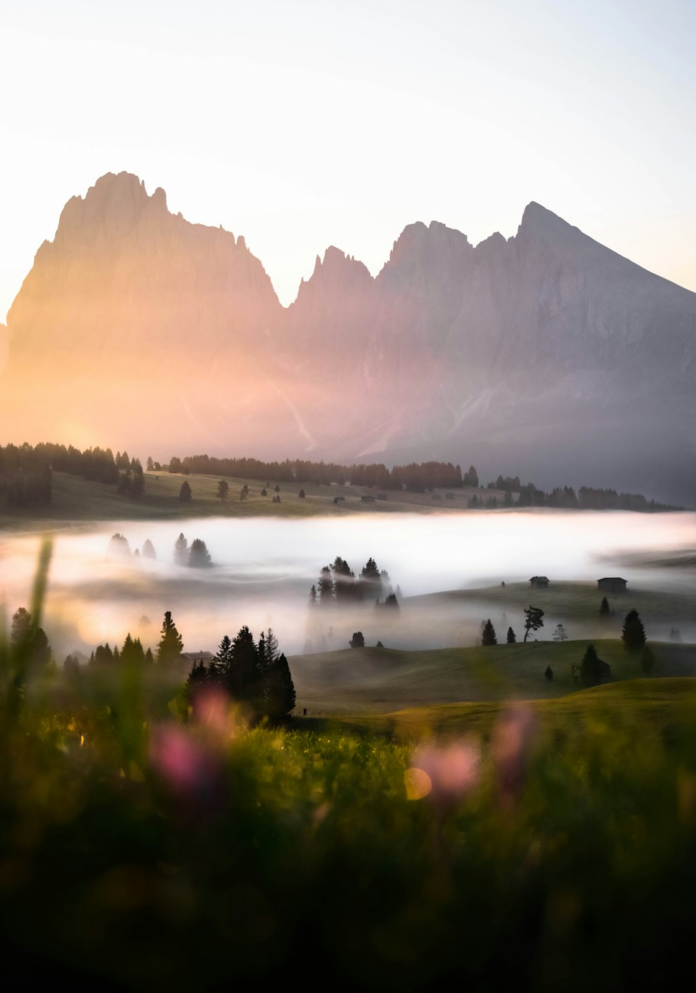 Sunlight illuminates mountain peaks over misty valley with cabins.