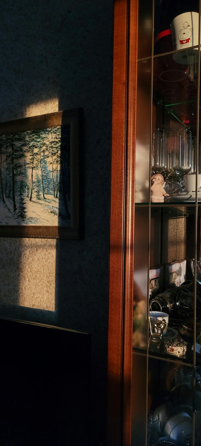 A landscape painting hangs above a glass wooden display cabinet.